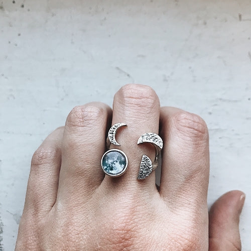 Hand wearing two silver rings with moon designs on a light background