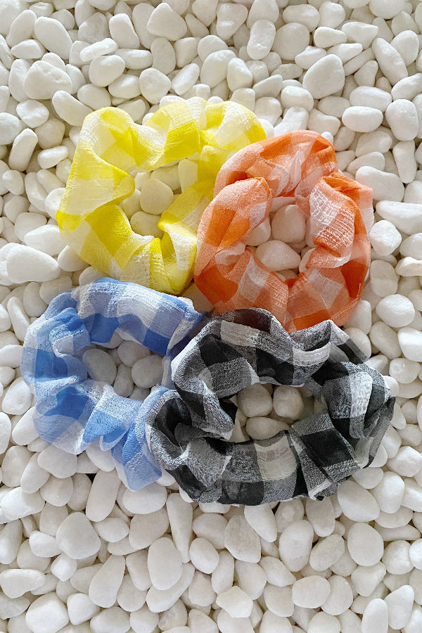 Four colorful scrunchies on a textured white surface