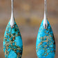 Turquoise teardrop earrings with silver hooks on a blurred background