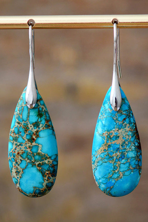 Turquoise teardrop earrings with silver hooks on a blurred background