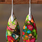 Colorful teardrop-shaped earrings hanging on a wooden stick against a brown background