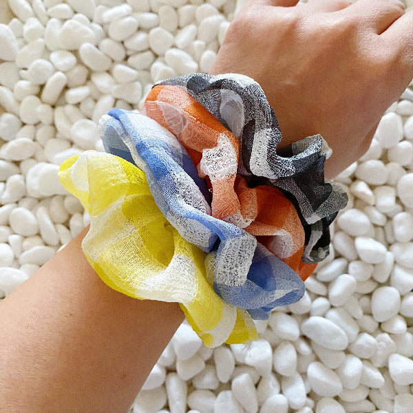 Colorful scrunchies on a wrist with a white pebble background
