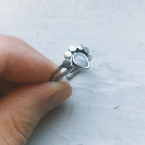 Silver ring with a blue stone on a finger against a light gray background
