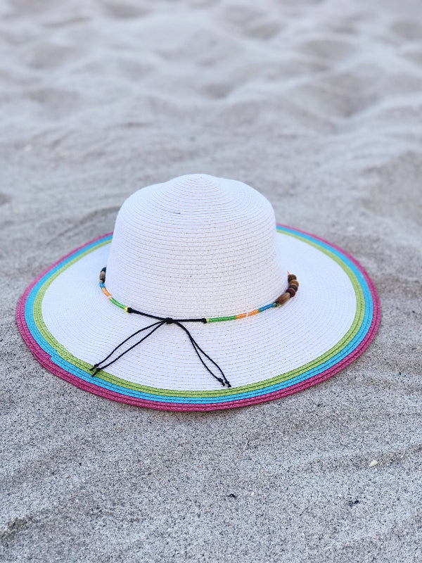 white and multicolor woven summer hat with beaded band resting on beach