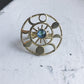 Gold circular pendant with a central blue gemstone on a textured white surface