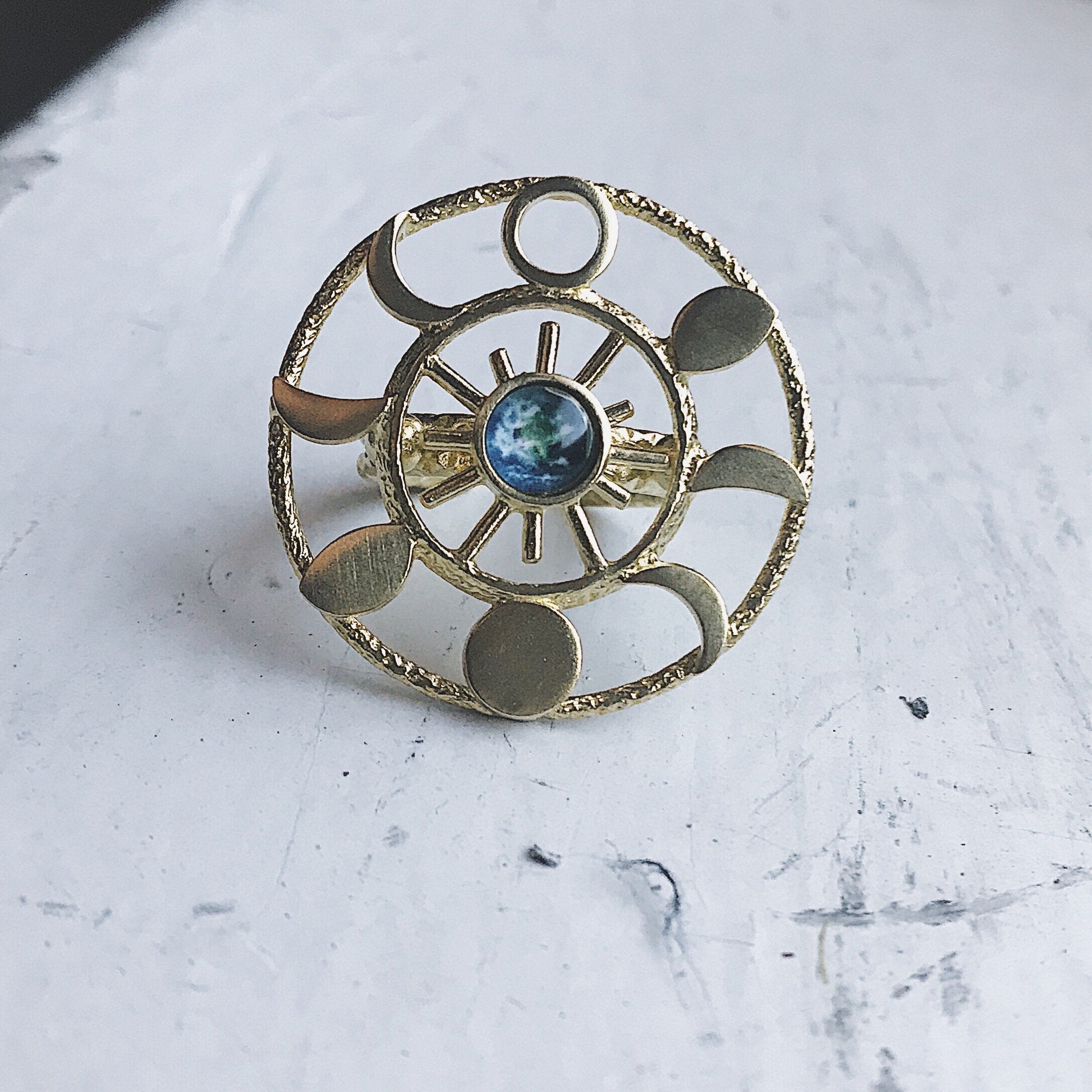 Gold circular pendant with a central blue gemstone on a textured white surface