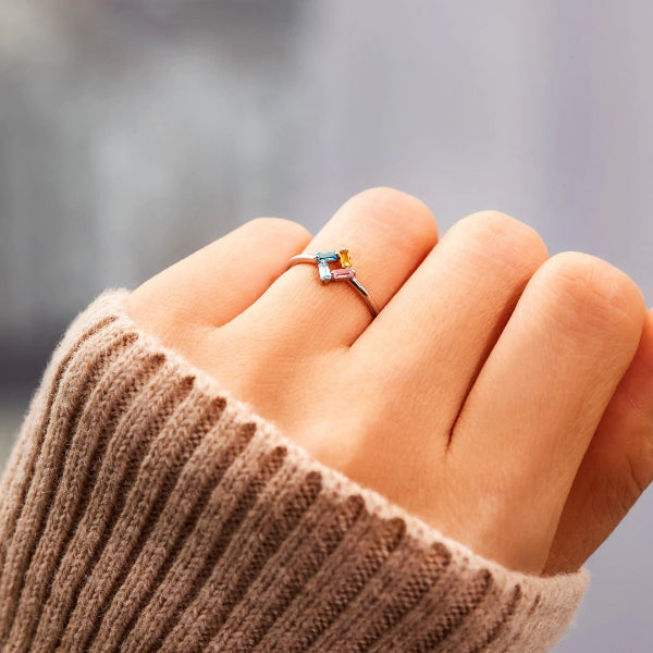 Close-up of a hand wearing a ring with a colorful gemstone against a blurred background