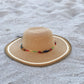 Tan woven summer hat with beaded band resting on beach