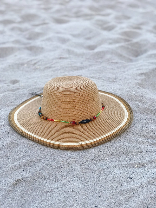 Tan woven summer hat with beaded band resting on beach