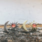 Pair of earrings with sun and moon designs on a wooden surface