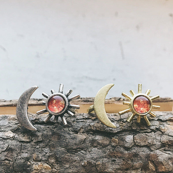 Pair of earrings with sun and moon designs on a wooden surface