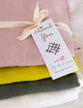 Stack of colorful fabric swatches with a 'thank you' tag on a light background