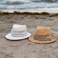 Two straw hats on a sandy beach with ocean waves in the background