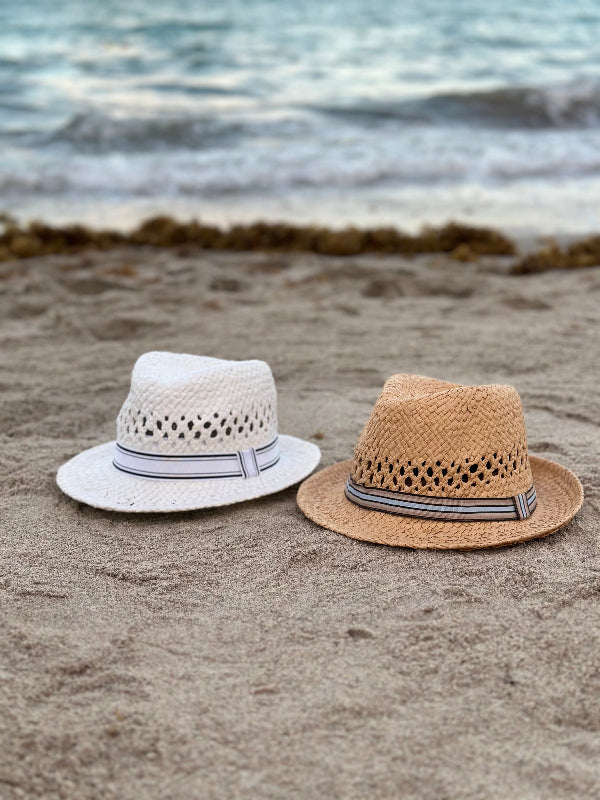Two straw hats on a sandy beach with ocean waves in the background