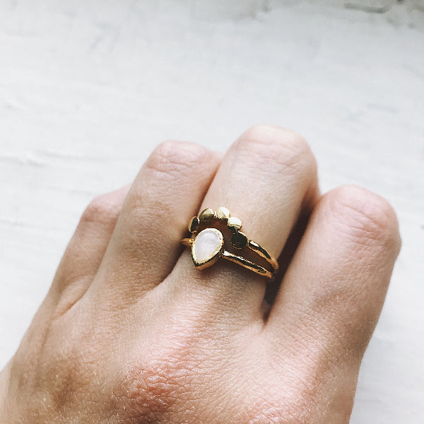 Gold ring with a central stone on a person's finger against a neutral background