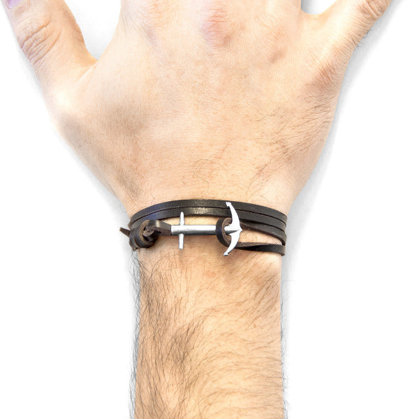 Hand wearing a black leather bracelet with a silver anchor charm on a white background
