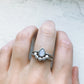 Silver ring with a teardrop-shaped gemstone on a finger against a light background