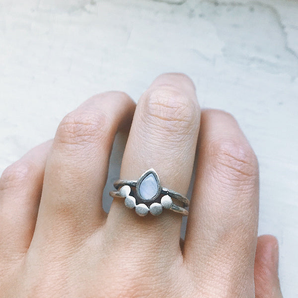 Silver ring with a teardrop-shaped gemstone on a finger against a light background