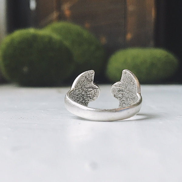 Silver cat ear-shaped ring on a white surface with a blurred green background