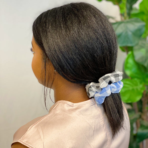Person with a ponytail using a checkered scrunchie against a neutral background