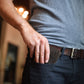 Person wearing a gray shirt and dark pants with a belt, standing indoors.
