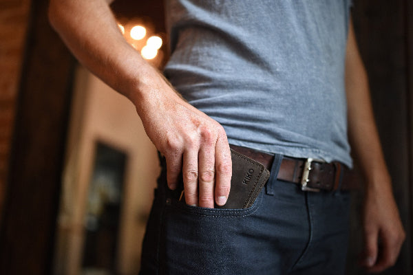 Person wearing a gray shirt and dark pants with a belt, standing indoors.