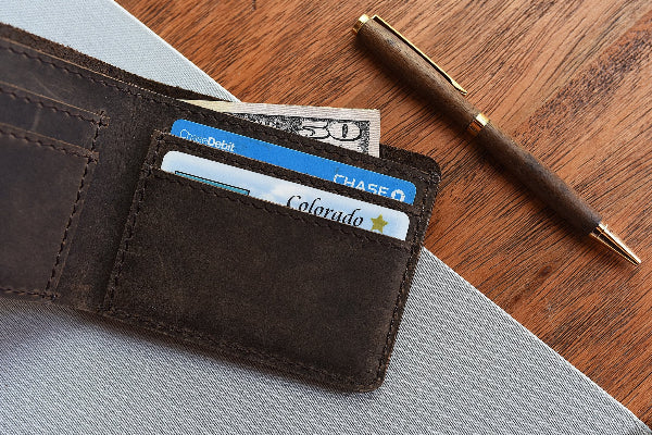 Brown leather wallet with cards and a pen on a wooden surface