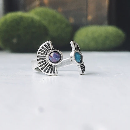 Silver ring with embedded stones on a white surface with greenery in the background
