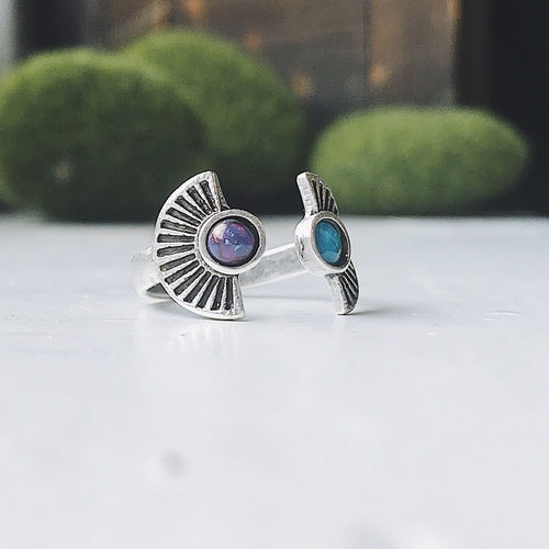 Silver ring with embedded stones on a white surface with greenery in the background