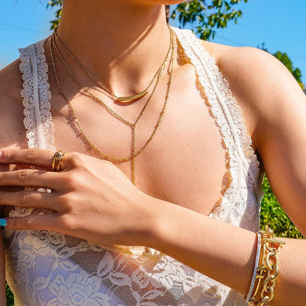Person wearing gold necklaces, bracelet, and ring with a blurred natural background
