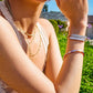 Close-up of a person wearing multiple necklaces and bracelets outdoors.