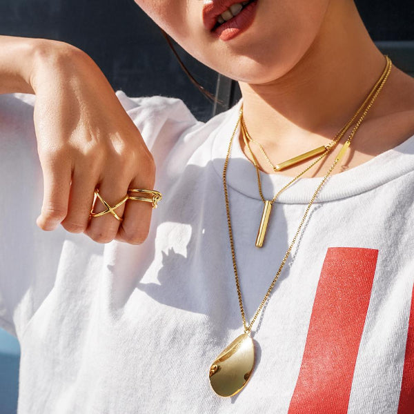 Person wearing gold necklaces and rings with a white shirt and red stripe.