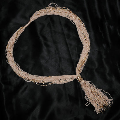 Beige headband with gold accents and tassel on a black background