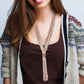 Woman wearing a patterned cardigan over a brown top with a decorative necklace.