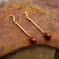 Gold earrings with red gemstones on a textured stone surface