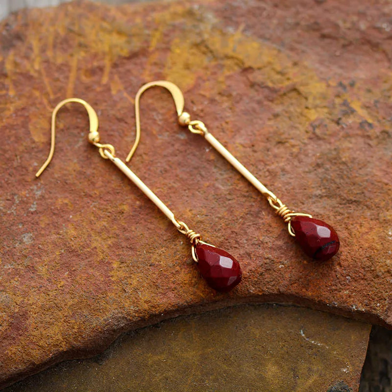 Gold earrings with red gemstones on a textured stone surface