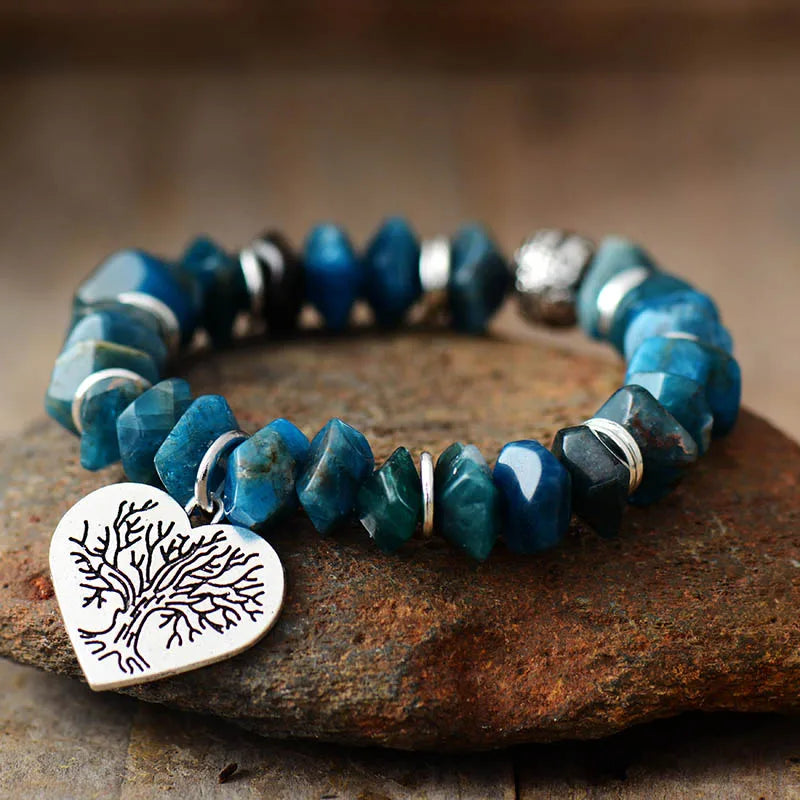 Blue beaded bracelet with a silver tree-shaped charm on a stone surface