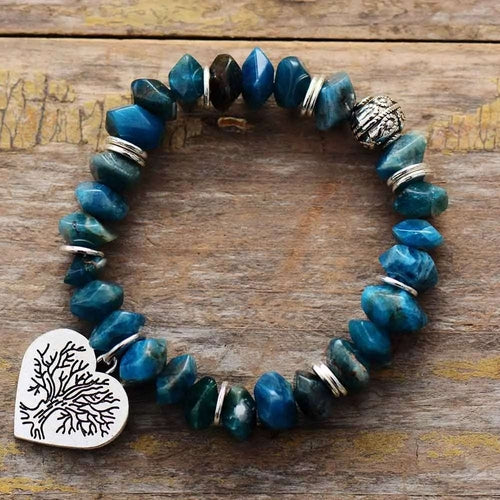 Blue beaded bracelet with a silver heart-shaped charm on a wooden surface
