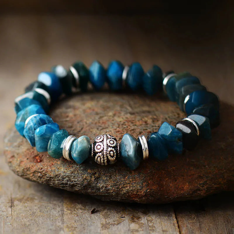 Blue beaded bracelet with a silver and gold accent on a stone surface