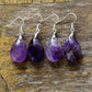 Four pairs of purple teardrop earrings on a wooden surface