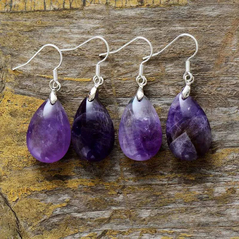 Four pairs of purple teardrop earrings on a wooden surface