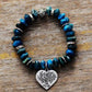 Blue beaded bracelet with a silver heart charm featuring a tree design on a wooden surface.