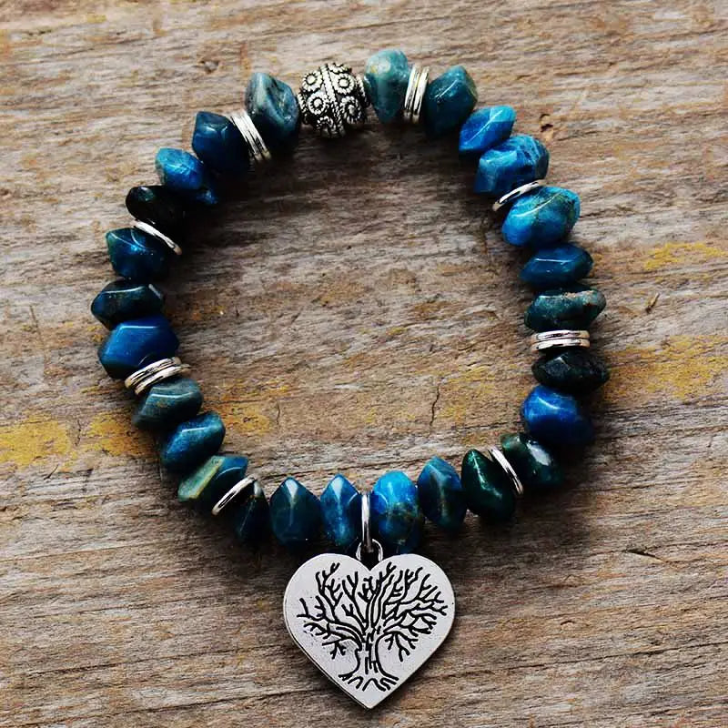 Blue beaded bracelet with a silver heart charm featuring a tree design on a wooden surface.