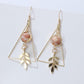 Gold triangle earrings with leaf details on a white background