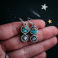 Pair of earrings with turquoise stones held between fingers against a dark background with star designs.