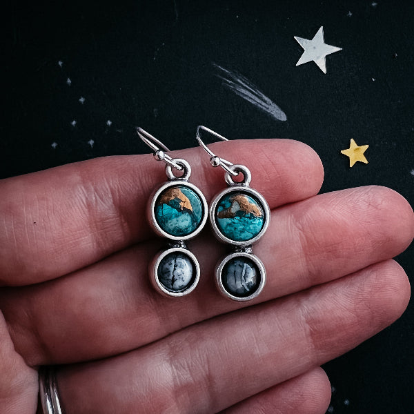 Pair of earrings with turquoise stones held between fingers against a dark background with star designs.