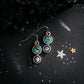 Pair of earrings with turquoise and moonstone stones on a dark surface with star decorations.
