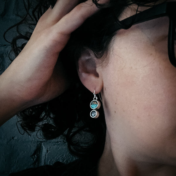 Close-up of a person wearing a silver earring with three circular stones.