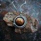 Silver pendant with a brown stone on a textured dark surface
