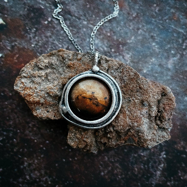 Silver pendant with a brown stone on a textured dark surface